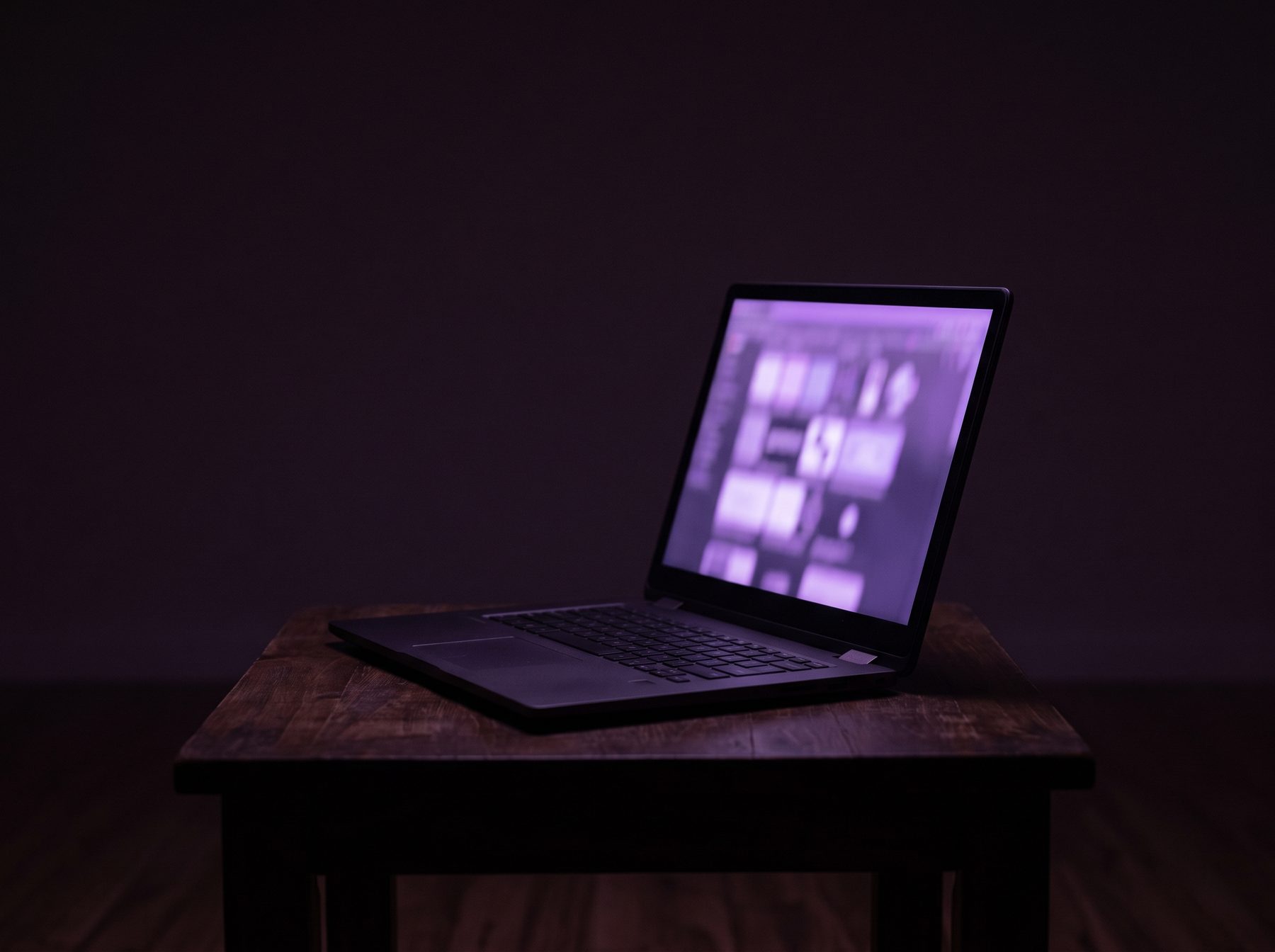 A laptop open in a dark room, its screen the brightest surface in the frame.